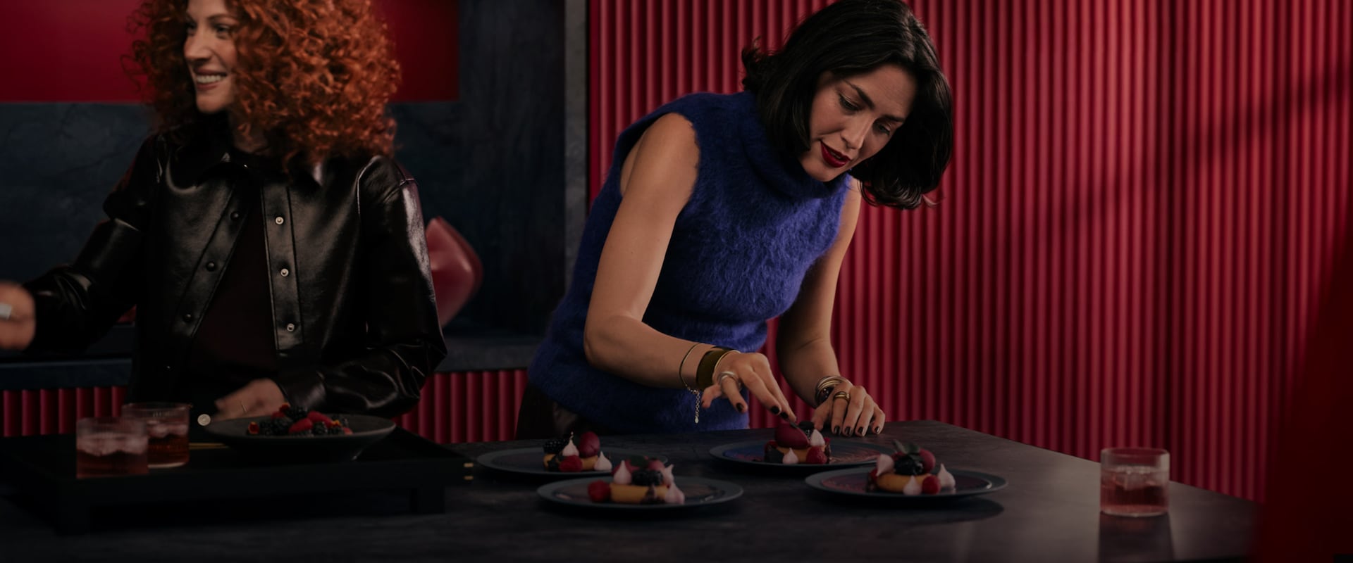 To kvinder forbereder desserter på en mørk køkkenø.